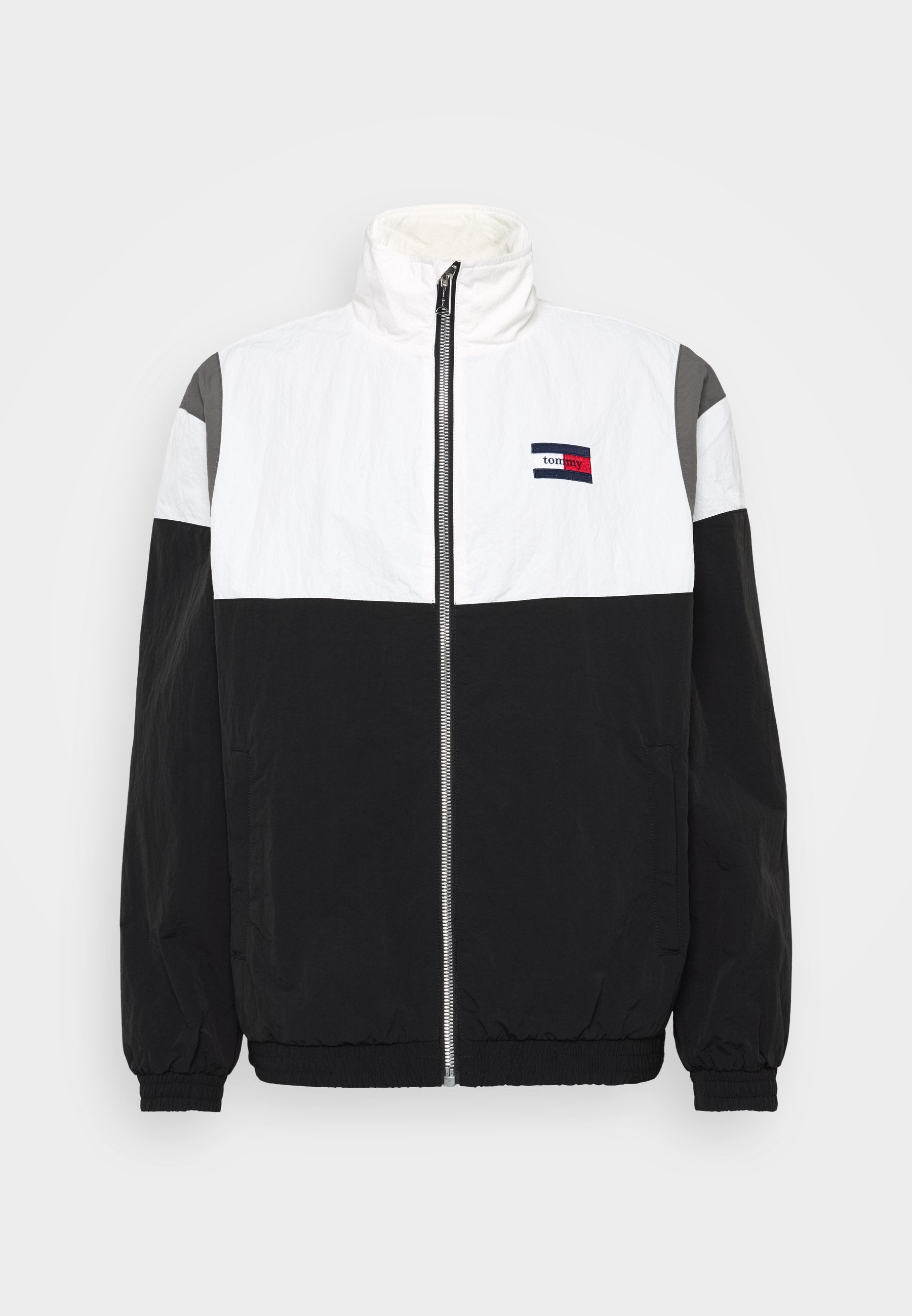 Schwarze, weiße und graue Windbreaker-Jacke mit hohem Kragen, Reißverschluss vorne, elastischen Bündchen und horizontalem Farbschema. Logo-Detail auf der Vorderseite.