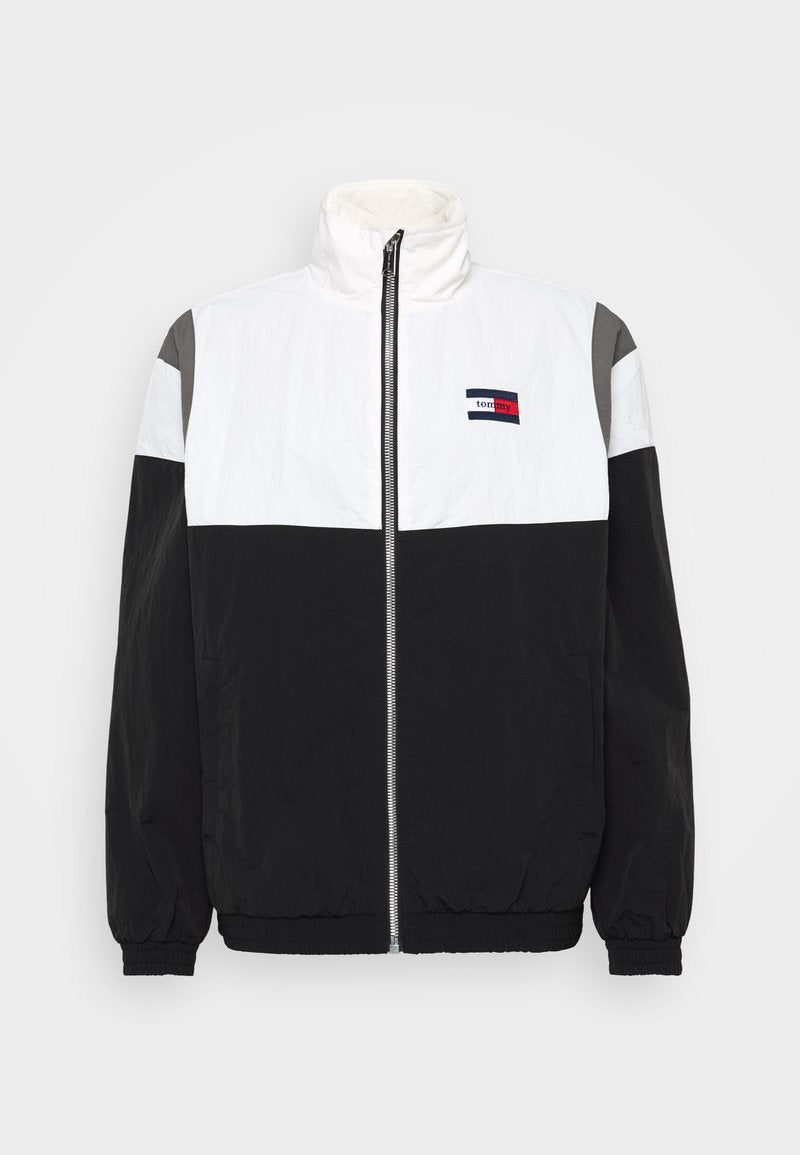 Schwarze, weiße und graue Windbreaker-Jacke mit hohem Kragen, Reißverschluss vorne, elastischen Bündchen und horizontalem Farbschema. Logo-Detail auf der Vorderseite.