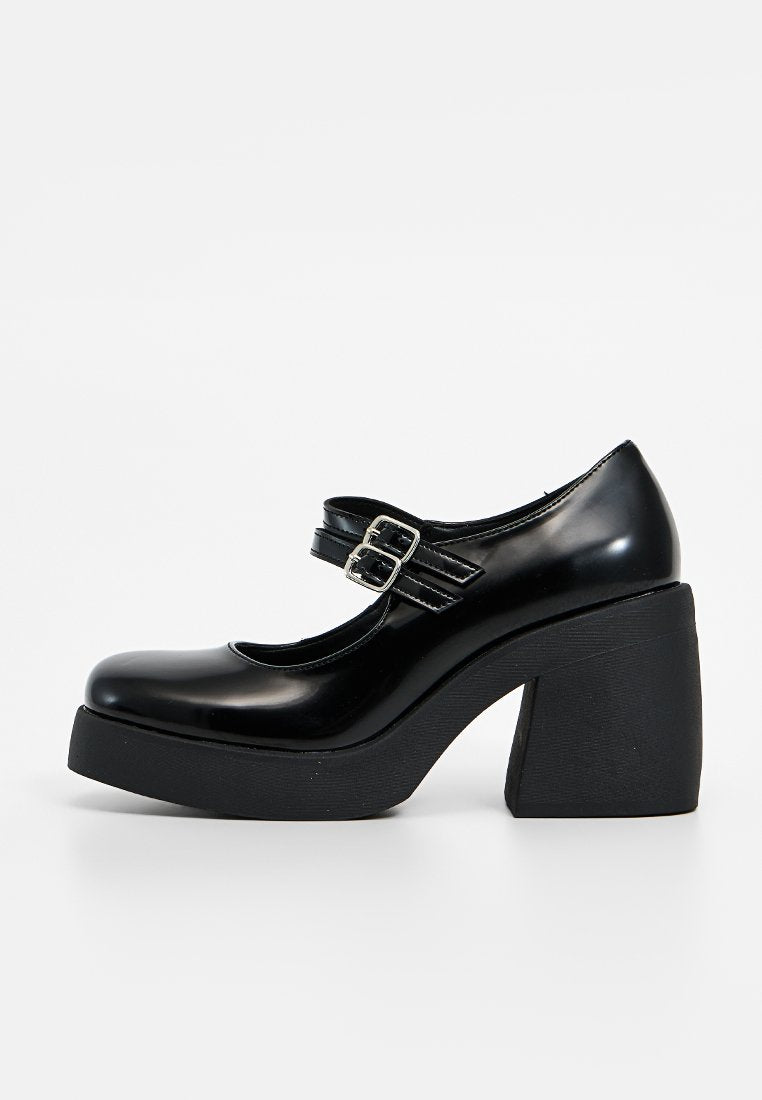 Schwarze patentierte Mid-Heels mit runder Spitze, Blockabsatz und doppelten Schnallenriemen über dem Spann. Glatte Textur mit glänzender Oberfläche.