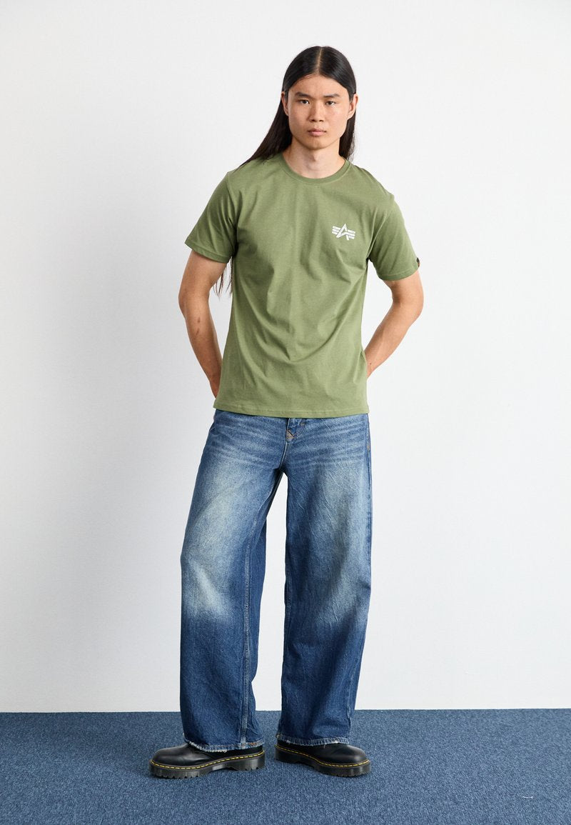 Olivgrünes T-Shirt mit kurzen Ärmeln, lockerer Schnitt, mit weißem Logo. Kombiniert mit weit geschnittenen blauen Jeans und schwarzen Plateaustiefeln. Minimalistisches Design.