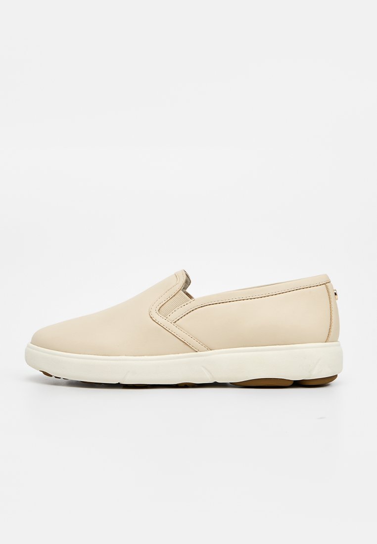 Beiger Slipper mit weißer Sohle, niedrigem Absatz und elastischen Seitenteilen für einfaches An- und Ausziehen und Komfort.