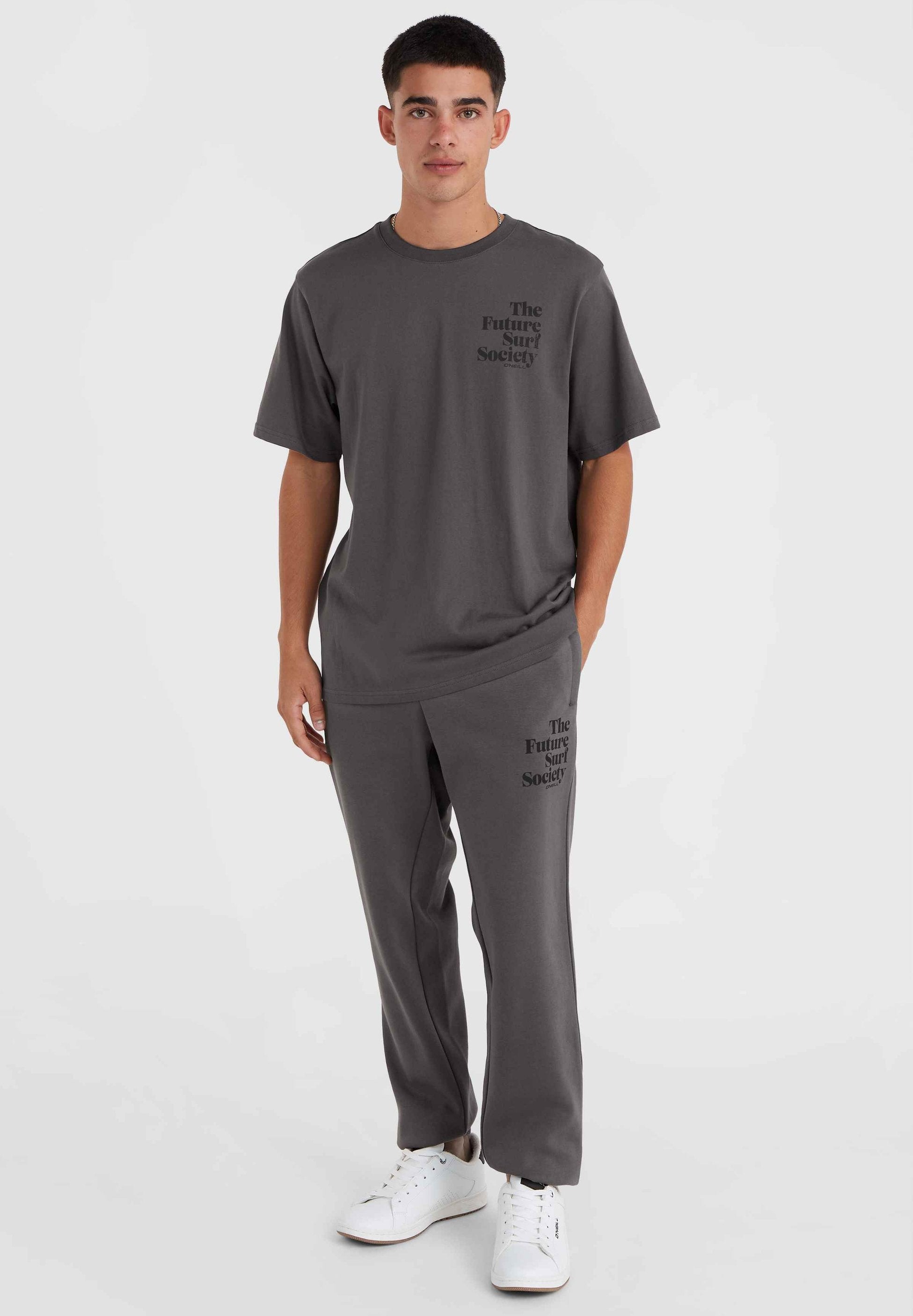 Grauer Baumwoll-T-Shirt und Sweatpants-Set mit dem Logo "The Future Surf Society", Rundhalsausschnitt, lockere Passform, kombiniert mit weißen Sneakers.