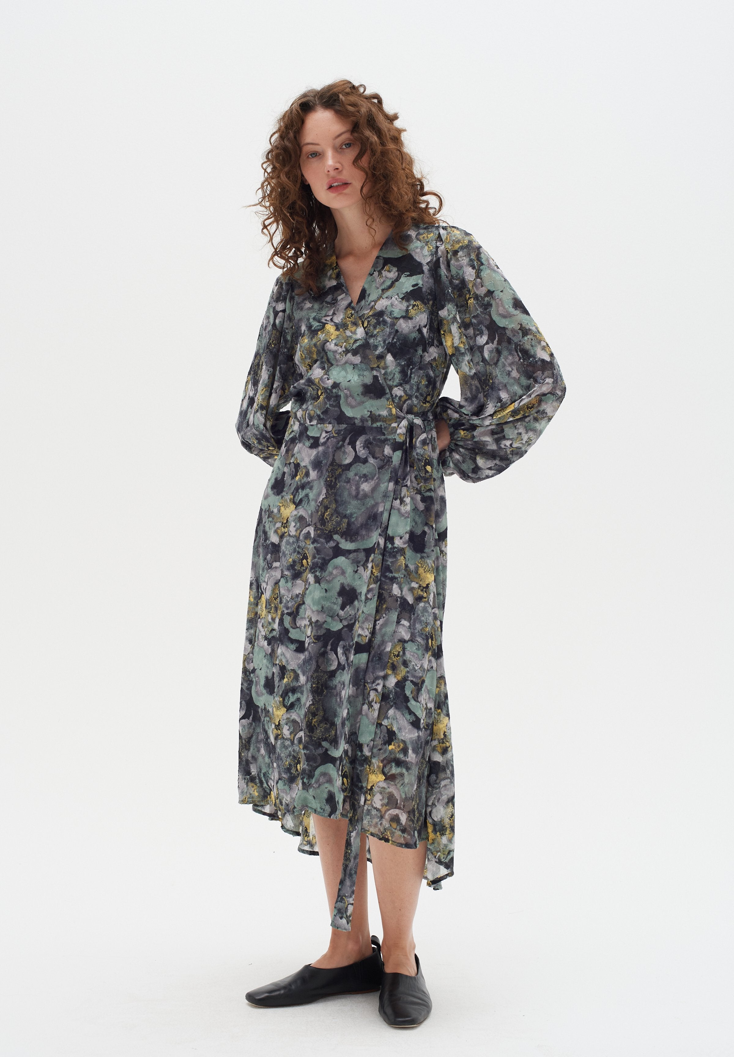 Florales Wickelkleid mit langen, ausgestellten Ärmeln, mit grünen, grauen und gelben Mustern, aus leichtem Stoff, mit einer Bindung an der Taille.
