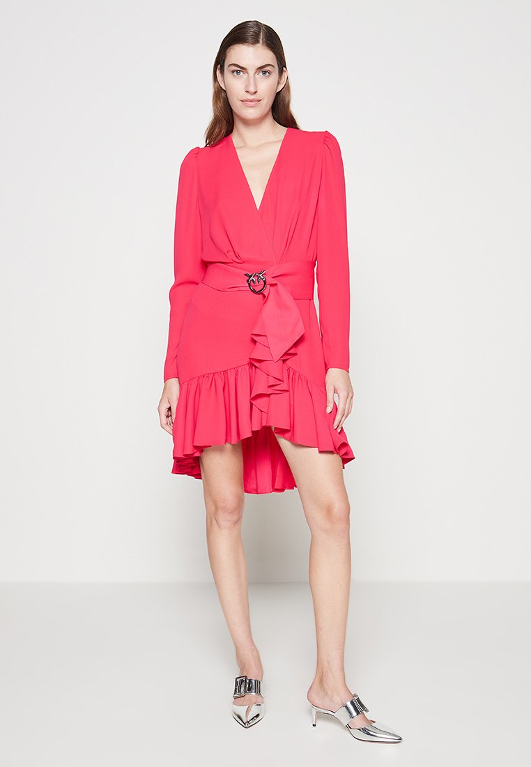 Rosa Wickelkleid mit langen Ärmeln, voluminösem Saum und einem Bindegürtel mit einem runden Verschluss. Abgerundet mit metallischen Absatz-Mules.