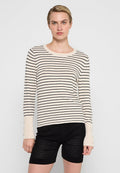 Beige gestreifter Pullover mit schwarzen horizontalen Streifen, rundem Ausschnitt, langen Ärmeln und Knopfdetails an den Bündchen, kombiniert mit strukturierten schwarzen Shorts.