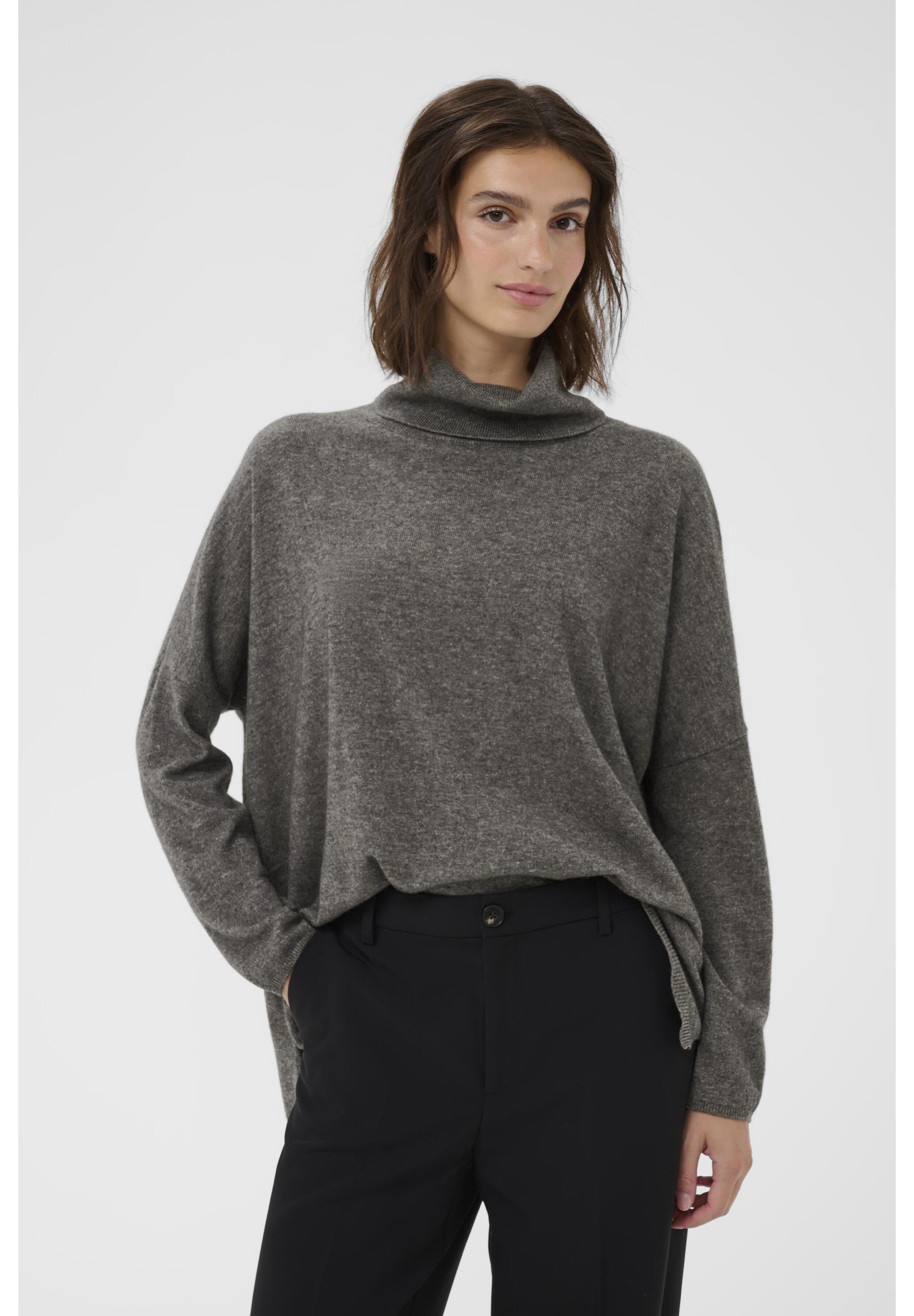 Hellgrauer, locker sitzender Pullover mit einem hohen, umgeschlagenen Kragen aus weichem Material, ausgestattet mit einem Seitenschlitz und langen Ärmeln, kombiniert mit schwarzen Hosen.