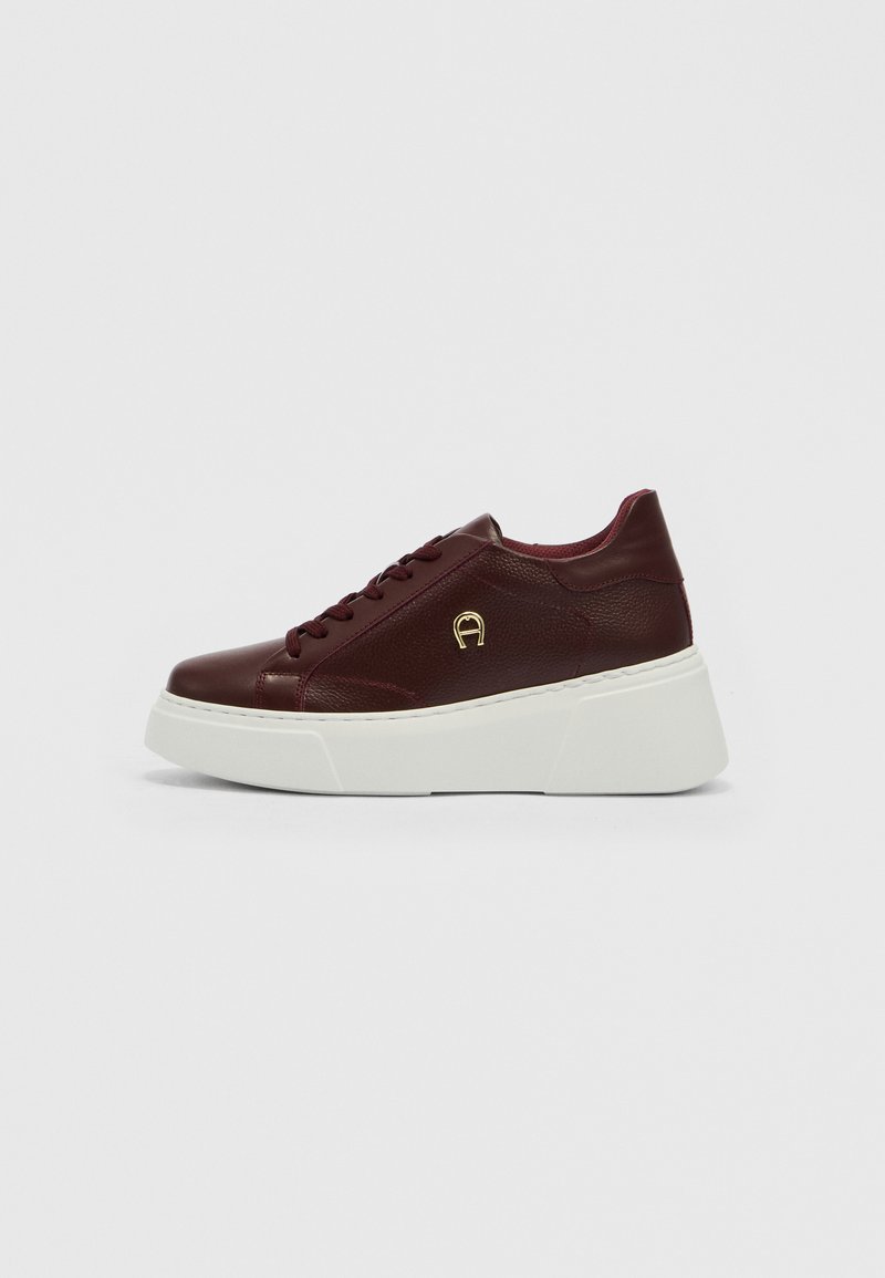 Sneaker aus burgunderfarbenem Leder mit dicker weißer Plateau-Sohle, Schnürung vorne und kleinem goldfarbenem Logo an der Seite.