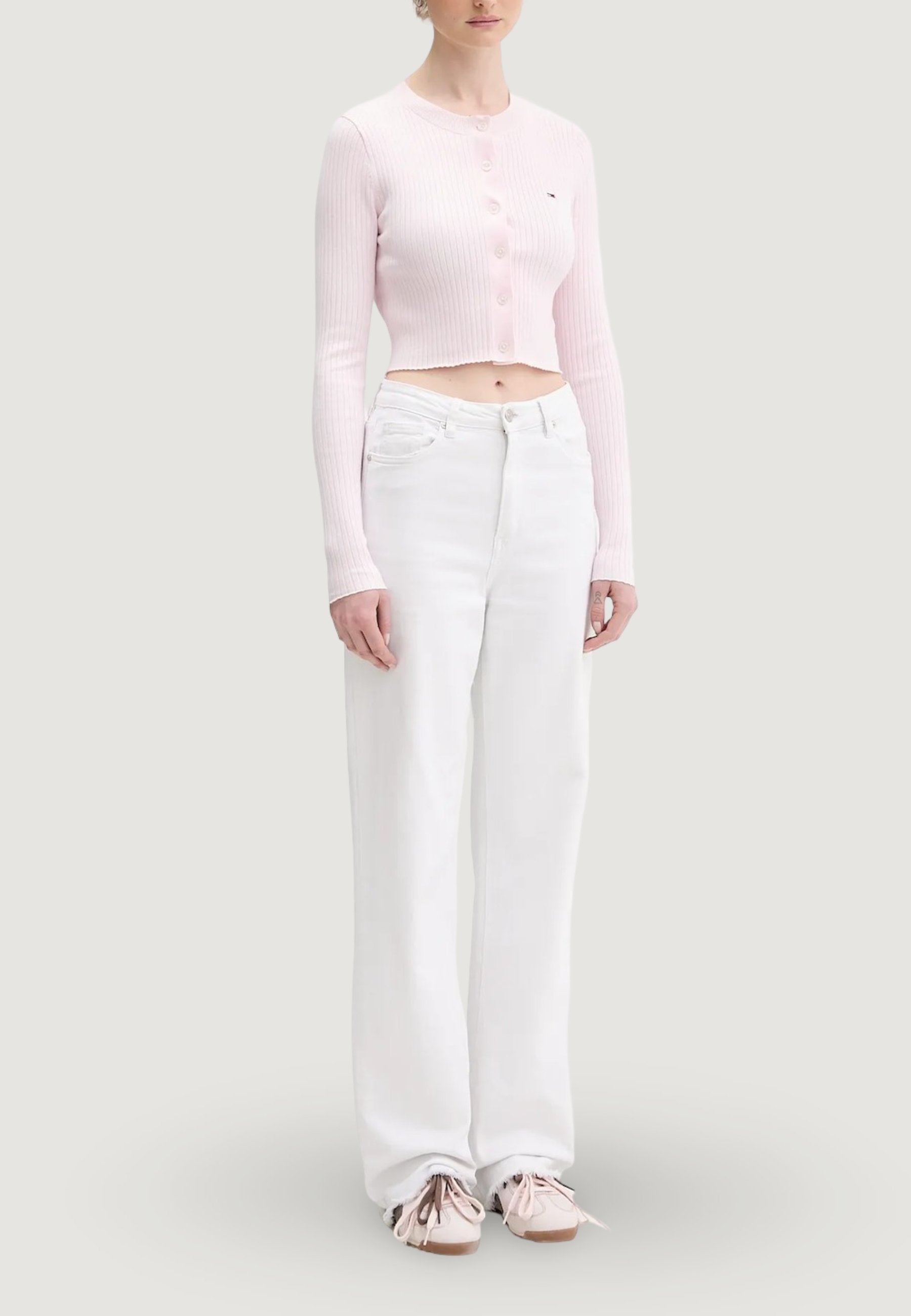 Helles rosa kurzes Strickjäckchen mit Rippenstruktur und Knöpfen, kombiniert mit weißen Jeans mit weitem Bein und hellrosa Schuhen mit braunen Sohlen und Bindebändern.