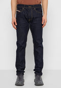 Dunkelblaue Jeans mit geradem Schnitt, gelben Nähten, fünf Taschen und einem Knopfverschluss. Getragen mit grauen Turnschuhen.