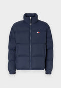 Marineblaue Steppjacke mit hohem Kragen, Reißverschluss und horizontalem Steppmuster. Mit einem kleinen Logo-Patch in Rot, Weiß und Blau.