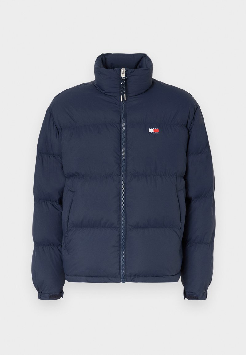 Marineblaue Steppjacke mit hohem Kragen, Reißverschluss und horizontalem Steppmuster. Mit einem kleinen Logo-Patch in Rot, Weiß und Blau.
