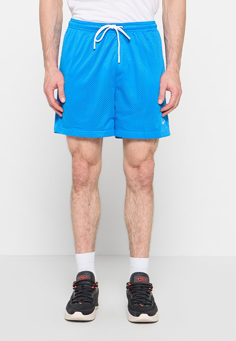 Mann trägt leuchtend blaue Netz-Sportshorts mit weißem Kordelzug, weiße Sportsocken und schwarze Turnschuhe, steht vor weißem Hintergrund.