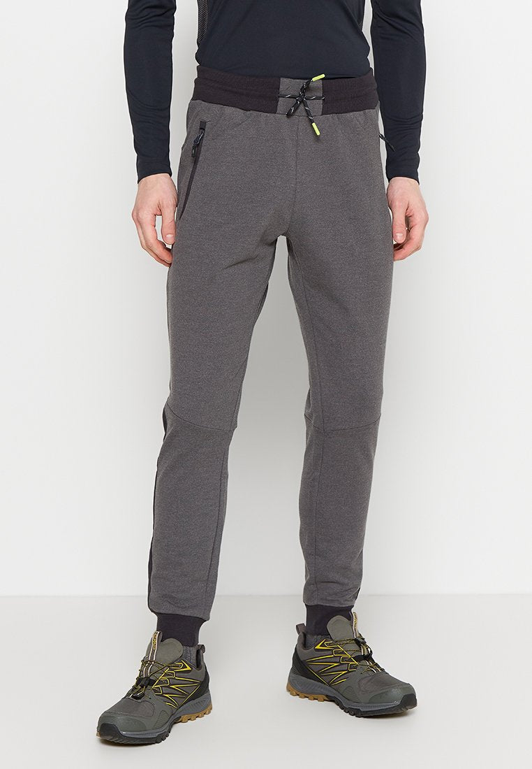 Mann trägt dunkelgraue Jogginghose mit Reißverschlusstaschen, schwarzen elastischen Bund mit Kordelzug, schwarzes Langarmshirt und graue Wanderschuhe.