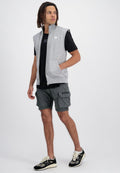 Graue ärmellose Zip-Weste über einem schwarzen T-Shirt, kombiniert mit dunkelgrauen Cargo-Shorts und schwarzen Sneakers mit weißen Akzenten und Taschen.
