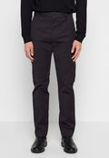 Mann in schwarzen Slim-Fit-Hosen, schwarzem Sweatshirt und schwarzen Lederstiefeln, der vor einem schlichten weißen Hintergrund steht.