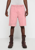 Rosa Shorts mit elastischem Bund, die eine strukturierte Oberfläche und ein knielanges Design aufweisen, kombiniert mit braunen Lederstiefeln mit Schnalle.