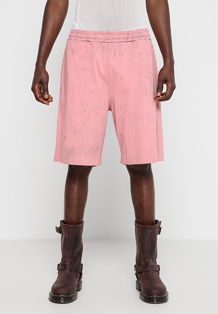 Rosa Shorts mit elastischem Bund, die eine strukturierte Oberfläche und ein knielanges Design aufweisen, kombiniert mit braunen Lederstiefeln mit Schnalle.