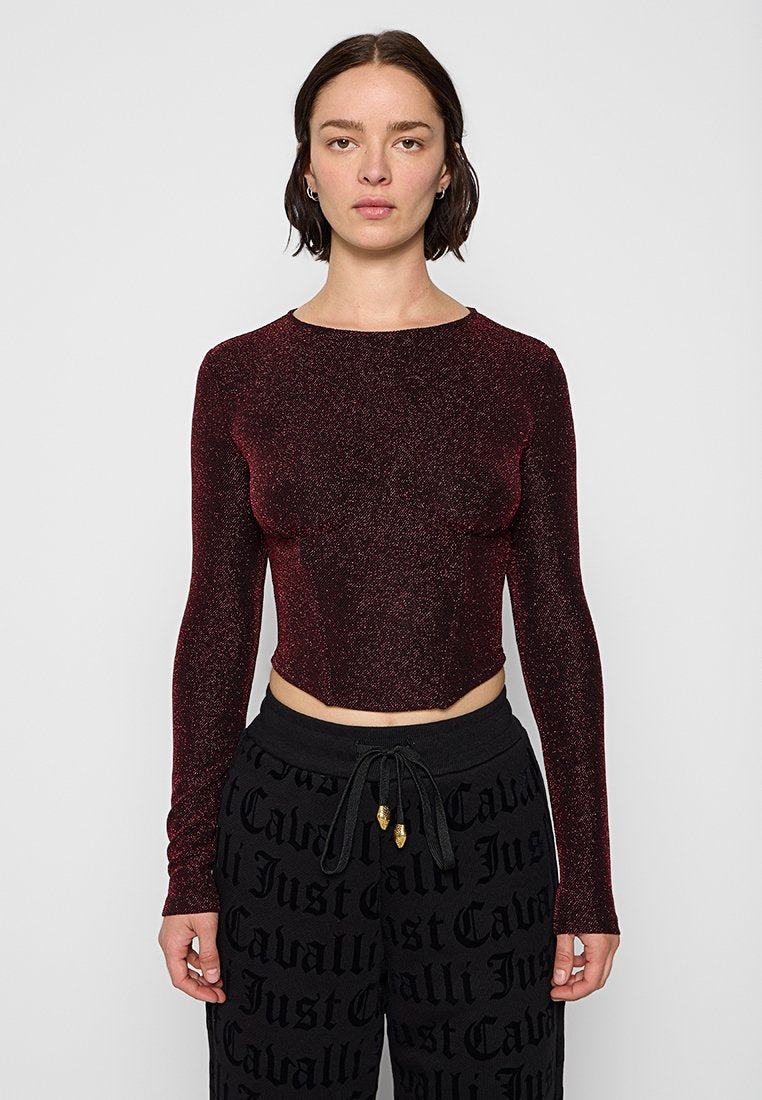 Frau in einem enganliegenden, langärmligen, schimmernden dunkelroten Crop-Top und schwarzen Jogginghosen mit auffälligem "Just Cavalli"-Textmuster.