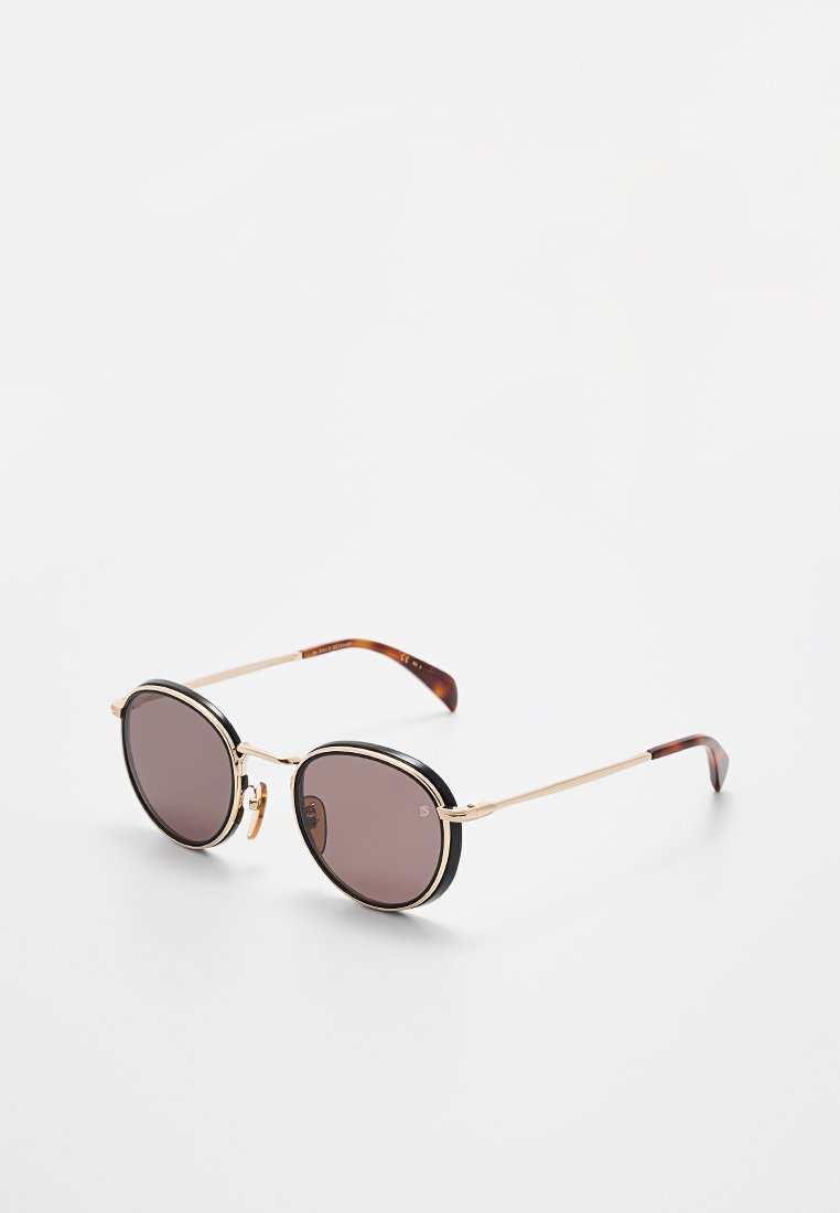 Runde Sonnenbrille mit dunkelbraunen Gläsern, dünnem goldfarbenem Metallgestell und Bügelspitzen im Schildpattmuster auf weißem Hintergrund.