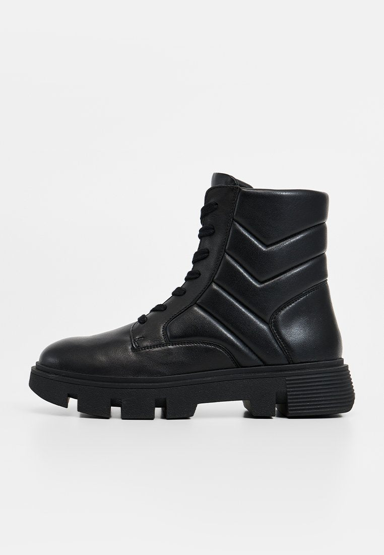 Schwarze Leder-Stiefeletten mit dicker Sohle, ausgestattet mit einer Schnürung und Chevron-Akzenten an den Seiten. Mattes Finish und robuste Bauweise.