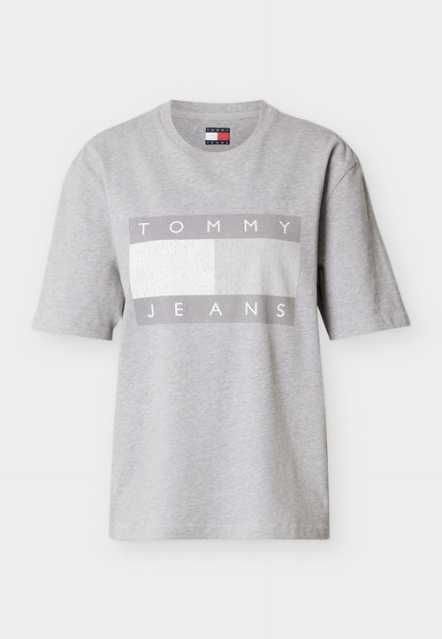 Graues T-Shirt mit kurzen Ärmeln aus Baumwolle, mit einem rechteckigen Motiv, das "TOMMY" in Weiß und "JEANS" in Grau auf einem strukturierten Hintergrund zeigt.