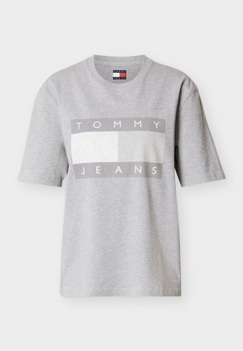 Graues T-Shirt mit kurzen Ärmeln aus Baumwolle, mit einem rechteckigen Motiv, das "TOMMY" in Weiß und "JEANS" in Grau auf einem strukturierten Hintergrund zeigt.