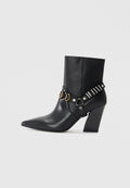 Schwarze Leder-Ankle-Boots mit spitzem Zehenbereich, gestapeltem Absatz und dekorativem Riemen mit Metallbeschlägen und Nieten. Glatte Textur.