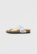 Weiße Flip-Flop-Sandale mit einem Korkfußbett, verstellbarem Riemen mit einer metallischen Schnalle und einer schwarzen Sohle; Branding an der Seite.