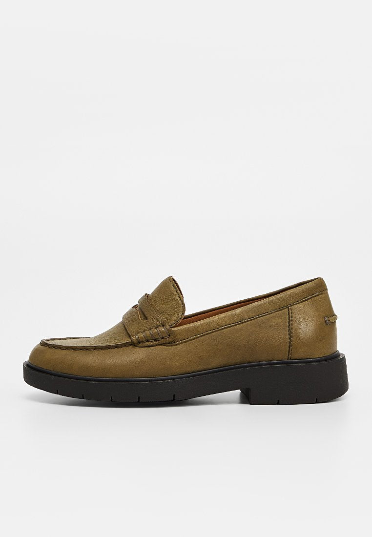 Brauner Leder-Slipper mit dicker schwarzer Gummisohle und Mokassin-Naht auf weißem Hintergrund.