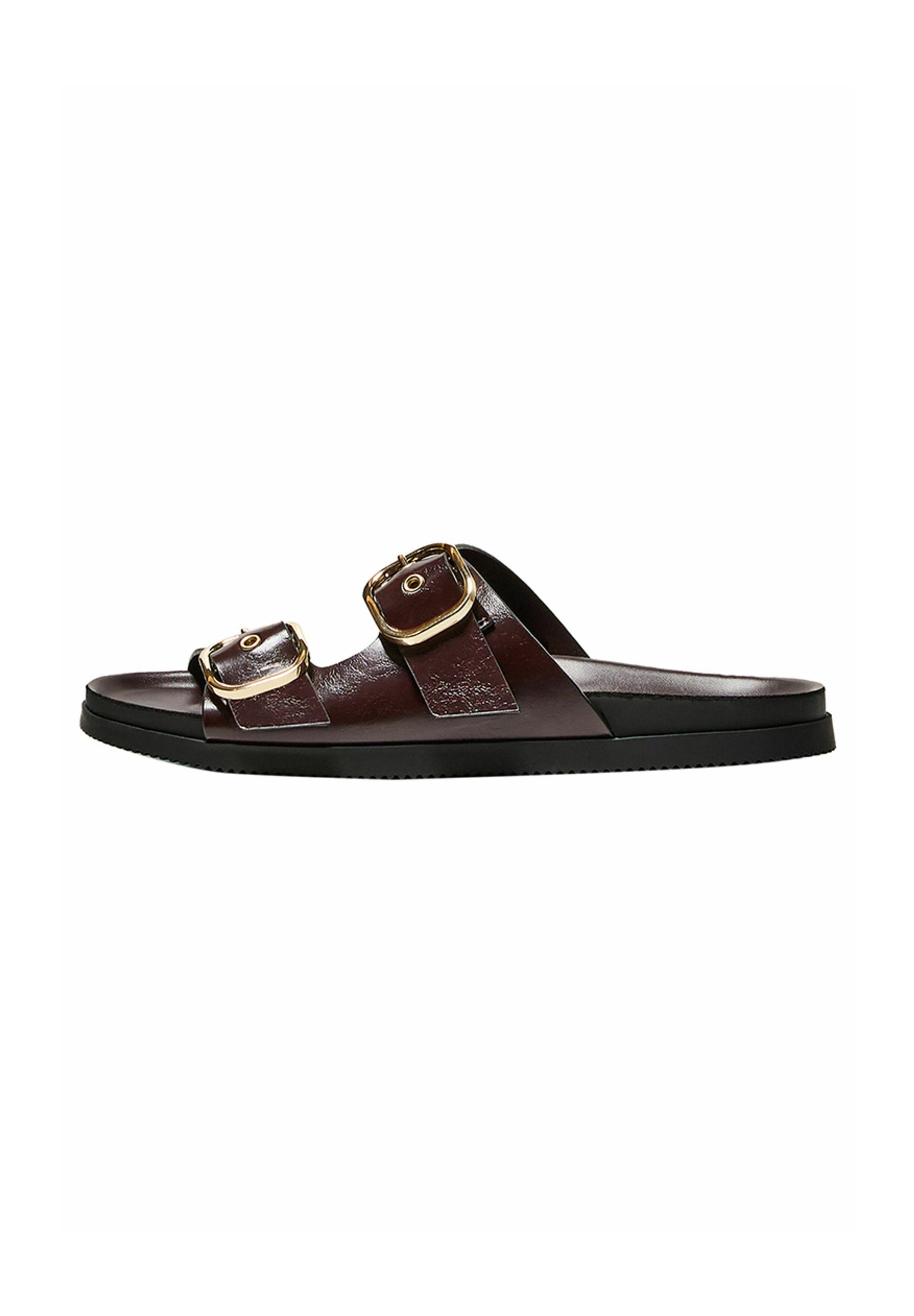 Braune Leder-Schlippersandalen verfügen über zwei verstellbare Riemen mit goldenen Schnallen, eine flache schwarze Sohle und eine glatte matte Oberfläche.