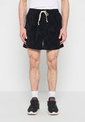 Mann trägt schwarze Shorts mit Kordelzug, weiße Socken und schwarze Sneaker, steht vor einfarbigem Hintergrund.