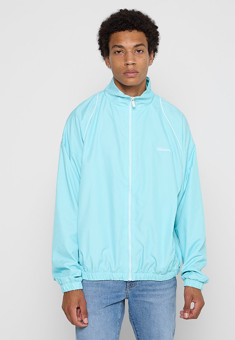 Helle blaue Windjacke mit hohem Kragen, Reißverschluss, elastischen Bündchen und Saum, mit einem dezenten Logo auf der Brust.