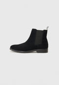 Schwarze Wildleder Chelsea-Boots mit elastischen Seiteneinsätzen und einer Zuglasche an der Ferse. Flache Sohle mit dezentem Branding an der Seite.