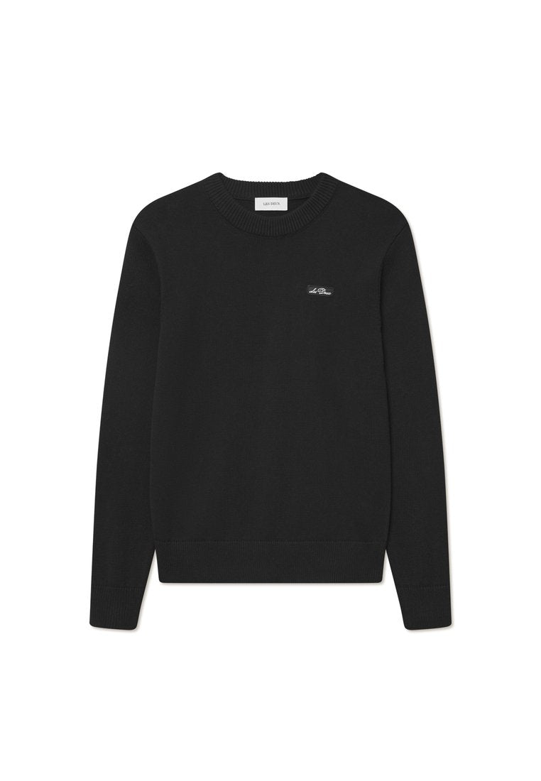 Schwarzer, gestrickter Pullover mit rundem Ausschnitt, gerippten Bündchen und Saum. Mit einem kleinen Logostick auf der Brust zur Markenkennzeichnung. Glatte Textur.