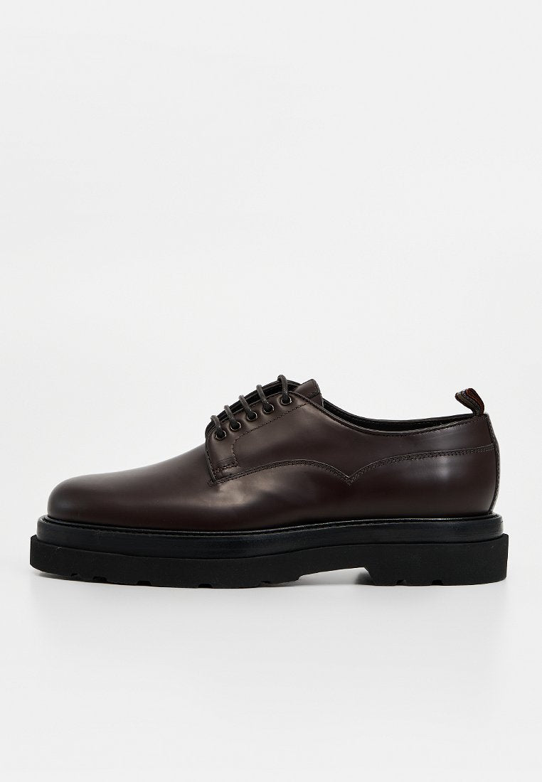 Brauner Lederschuh mit abgerundeter Spitze, Schnürung vorne und schwarzer, klobiger Sohle. Verfügt über dezente Nähte und eine Schlaufe an der Ferse.