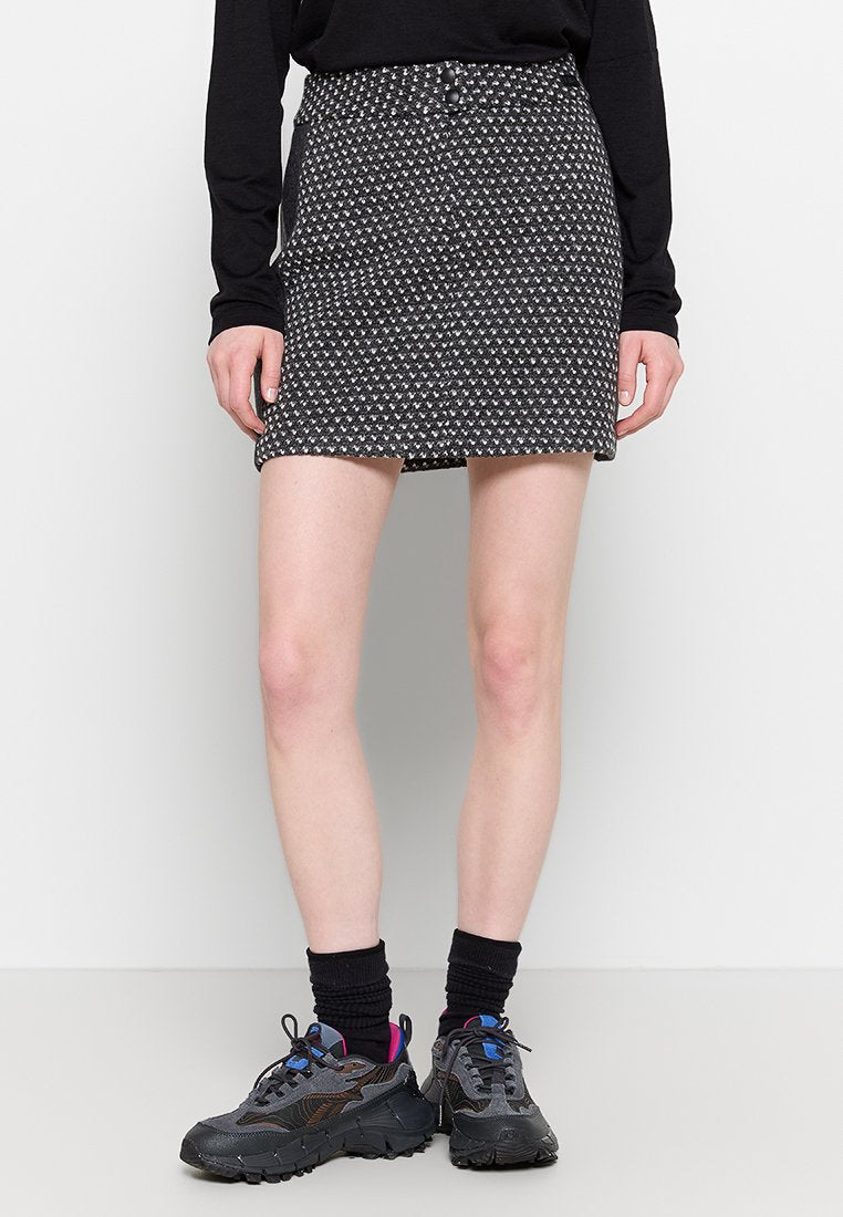 Schwarzer und weißer gemusterter Denim-Rock mit hoher Taille, vorderen Knöpfen und leichtem A-Linien-Schnitt, kombiniert mit grauen Sneakers und schwarzen Socken.