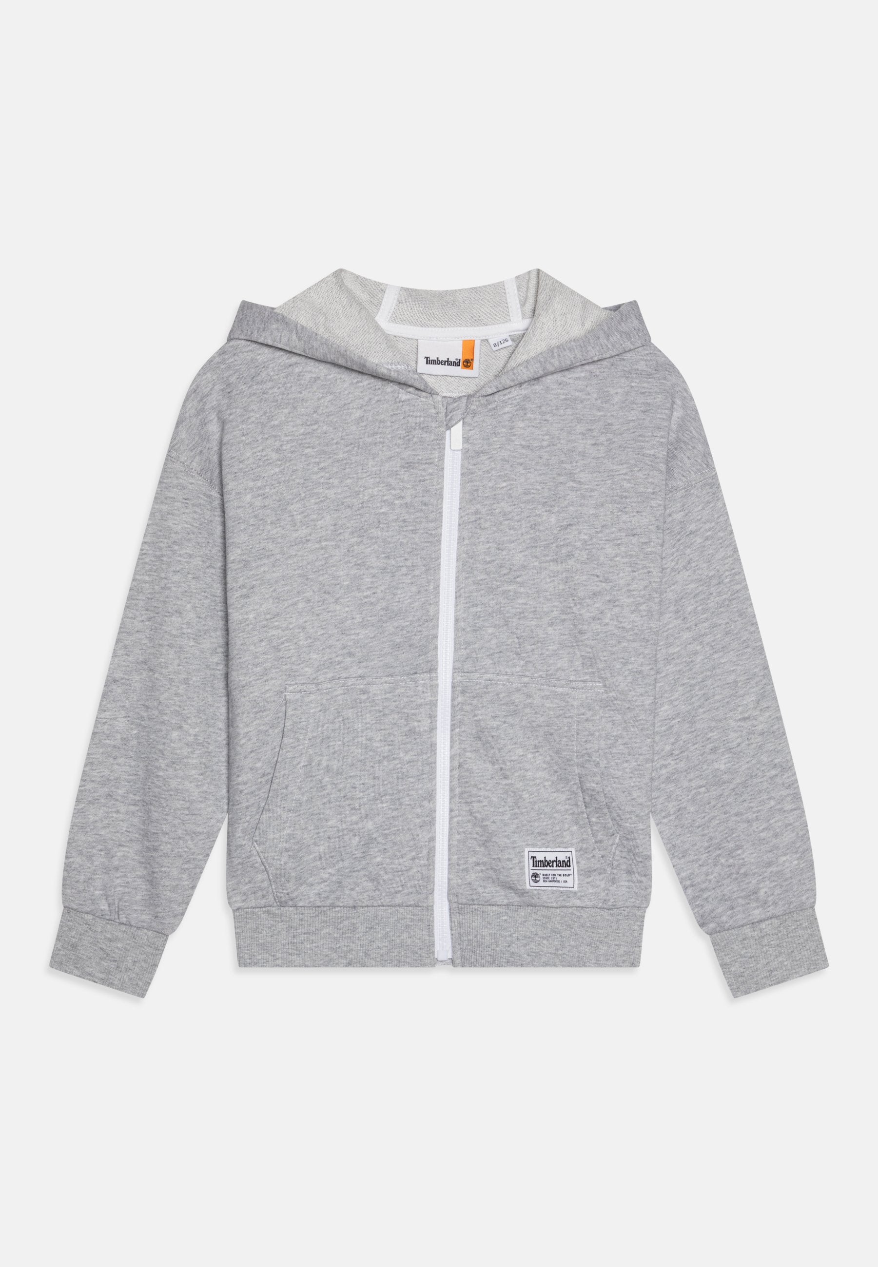 Grauer Kapuzenpullover mit Frontreißverschluss und zwei Seitentaschen. Mit gerippten Bündchen und einem weißen Etikett auf der unteren linken Seite. Weicher Stoff.
