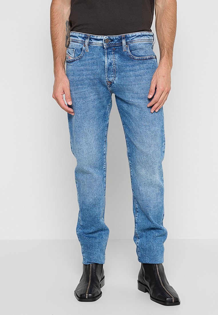 Blaue Denim-Jeans mit geradem Bein, kontrastierenden Nähten, Vorder- und Gesäßtaschen sowie mittelhoher Taille. Getragen mit schwarzen Knöchelstiefeln.