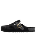 Schwarze, mit Fell überzogene Clogs mit einem schwarzen Lederriemen und einer goldenen Metallschnalle, die ein strukturiertes Muster und eine robuste schwarze Sohle aufweisen.