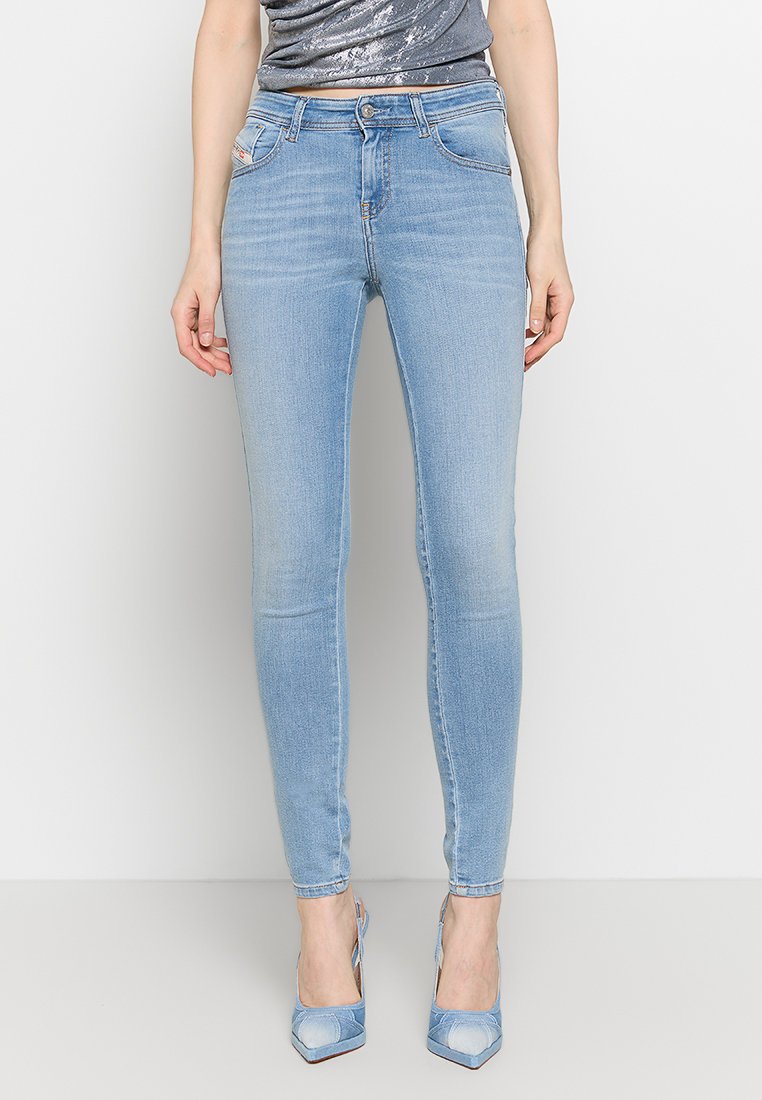 Hellblaue Denim-Skinny-Jeans mit leichter Ausbleichung, Fünf-Taschen-Design und Reißverschluss. Kombiniert mit einem grauen Oberteil und hellblauen Absätzen.