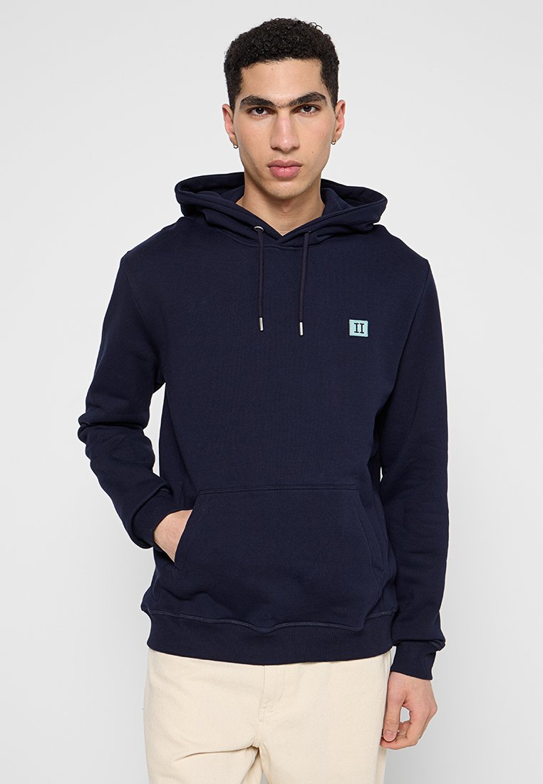Marineblaue Kapuzenjacke aus weichem Stoff, mit einer vorderen Tasche, Kordeln und einem kleinen hellblauen Logo auf der Brust.