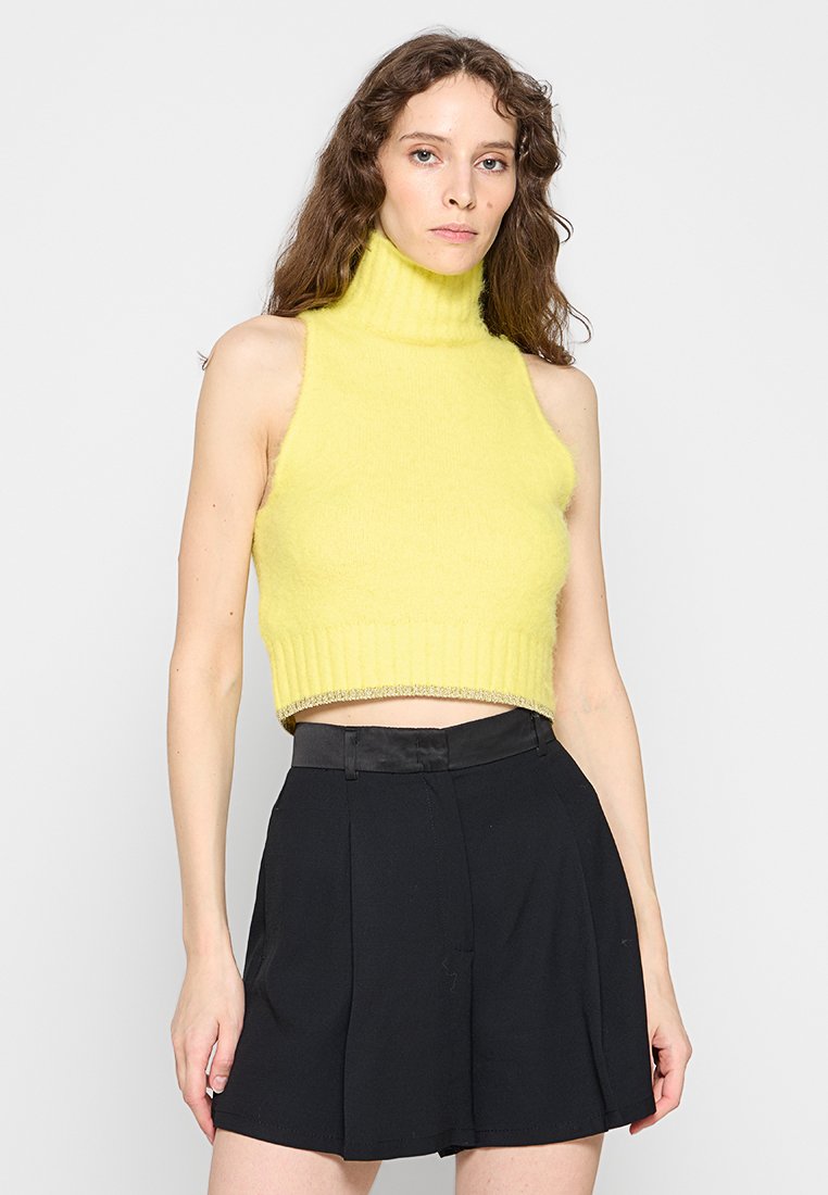 Gelbes ärmelloses Crop-Top mit Rollkragen aus weichem, flauschigem Material, mit Rippendesign und glitzerndem Saum, kombiniert mit schwarzen Shorts.