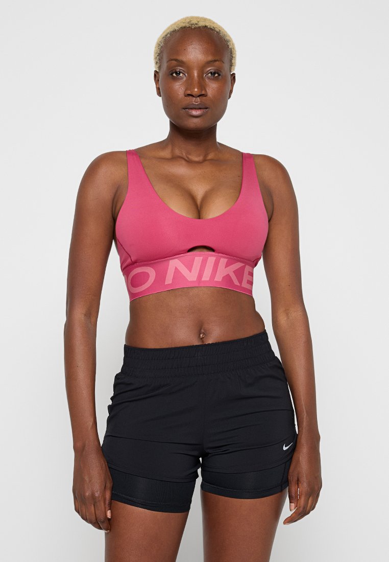 Pinkes Sport-BH mit breitem Bund und dem Schriftzug „NIKE“ in Hellpink; kombiniert mit schwarzen Sportshorts mit elastischem Bund und Logo.