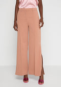 Pfirsichfarbene weit geschnittene Hose aus weichem Stoff mit seitlichen Schlitzen; verfügt über eine hohe Taille und FaltenDetails, ergänzt durch glänzende pinkfarbene Schuhe.