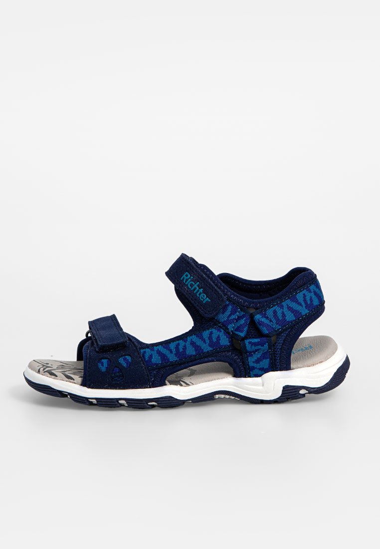 Marineblaue Sandalen mit einem gemusterten Textil-Obermaterial und verstellbaren Riemen. Leichte Sohle mit einem strukturierten Fußbett und weißen Sohlenakzenten.