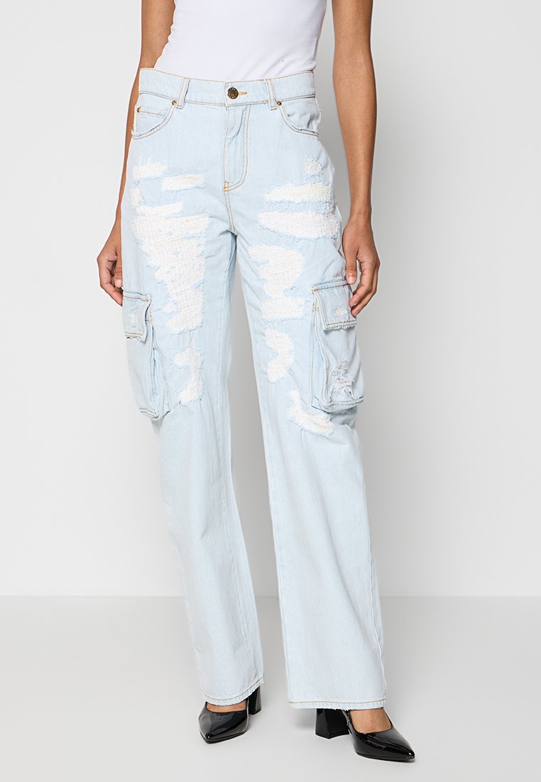 Helle blaue, beschädigte Cargo-Jeans mit Patch-Details, Frontklappen-Taschen, geradem Bein, kombiniert mit schwarzen Blockabsatzschuhen und einem weißen Oberteil.