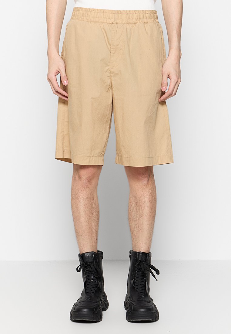 Beige Shorts mit einem elastischen Bund, aus leichtem Stoff gefertigt. Sie haben eine lockere Passform, ein knie-langes Design und keine sichtbaren Taschen.