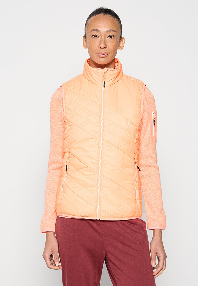 Leichte, ärmellose Weste in Pfirsich, mit diagonaler Steppung, Reißverschlusstaschen und hohem Kragen. Kombiniert mit einem rosa Langarmshirt.