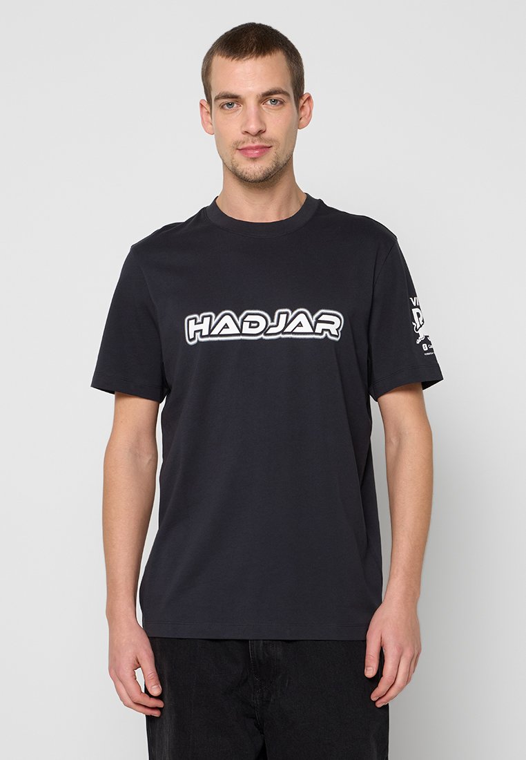 Schwarzes Baumwoll-T-Shirt mit Rundhalsausschnitt. Auf der Vorderseite befindet sich ein weißes "HADJAR"-Logo und auf dem linken Ärmel ein zusätzlicher Text.