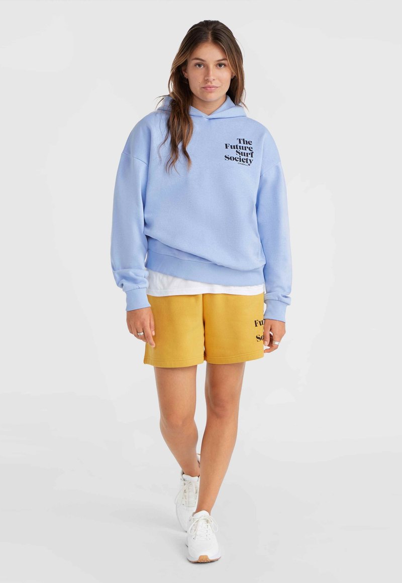 Hellblauer Hoodie mit dem Aufdruck "The Future Surf Society" in Schwarz, kombiniert mit gelben Shorts, die ein ähnliches Logo tragen, und weißen Sneakern.